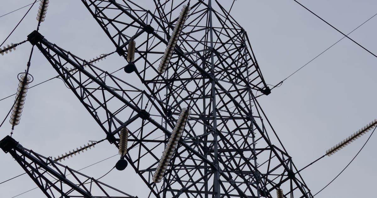 A steel electricity transmission tower seen from below against a pale sky
