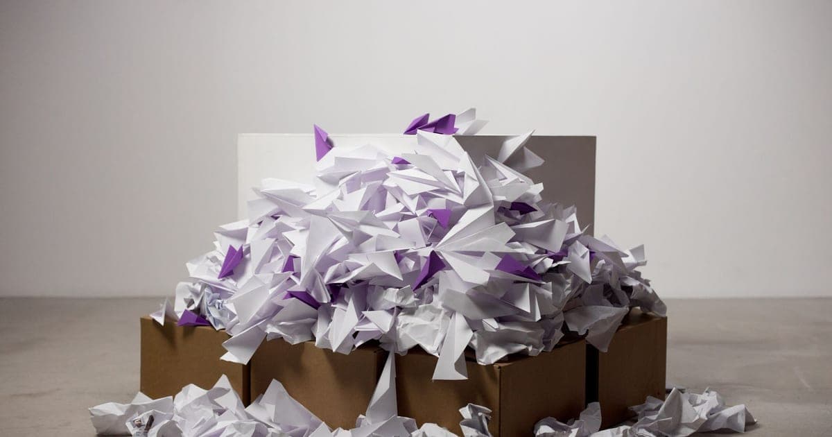 A cardboard box overflowing with paper planes and crumpled paper spilling onto the floor