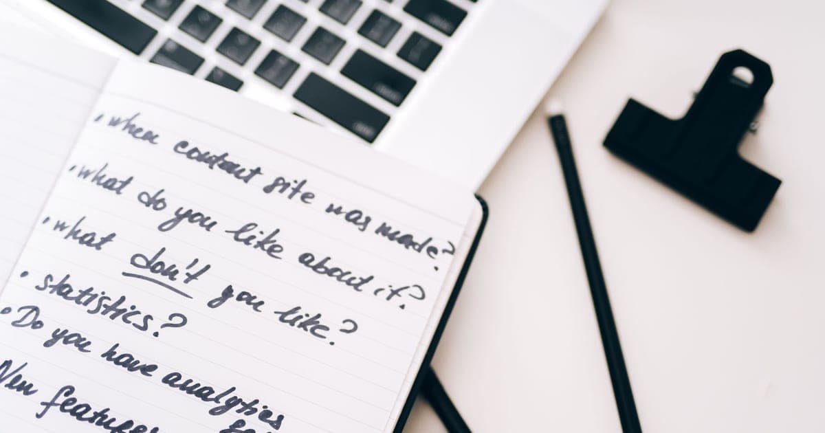 A notebook of handwritten questions resting on a laptop keyboard beside two pencils