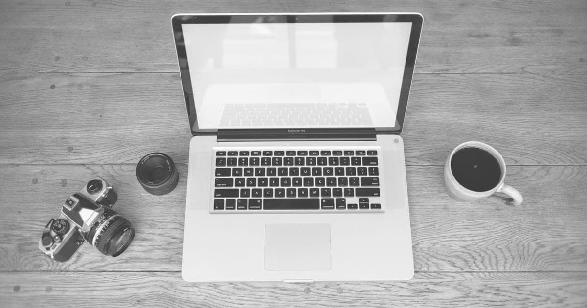 An open laptop on a wooden desk beside a camera and a coffee cup
