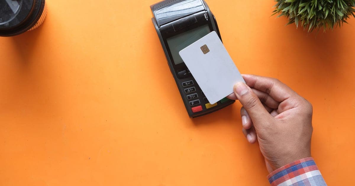 A hand holding a blank payment card up to a card terminal