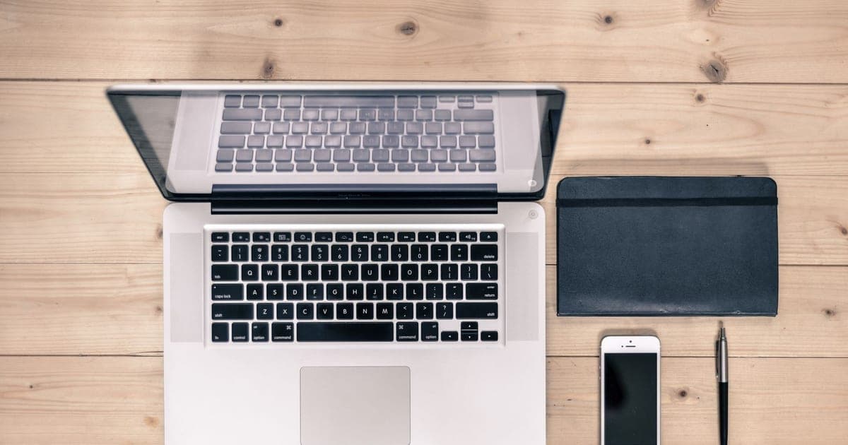 A tidy desk seen from above with an open laptop, a smartphone and a notebook