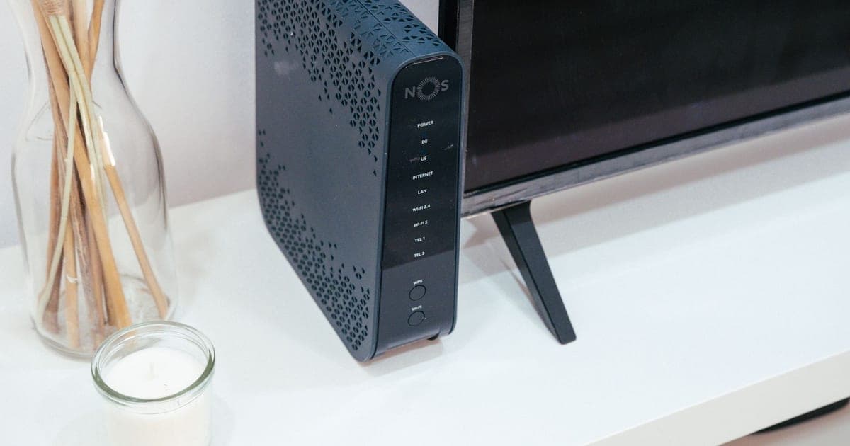 A black home router standing beside a monitor and a reed diffuser