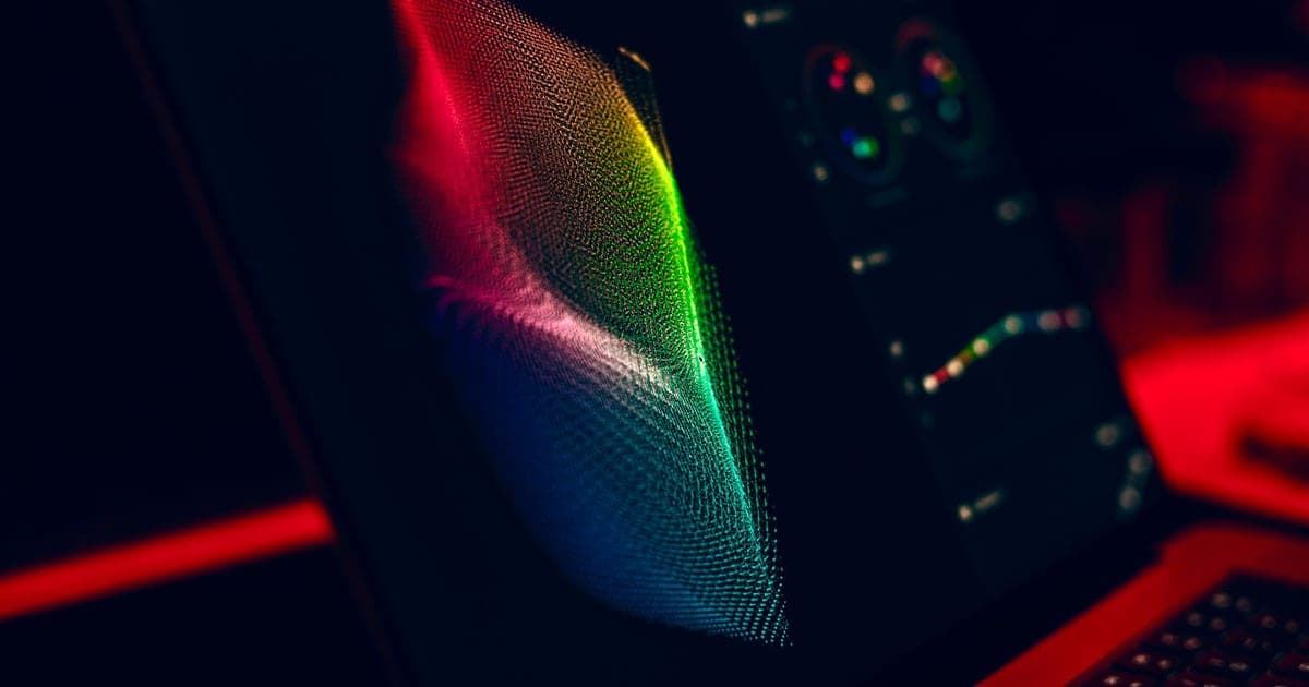 A dark monitor displaying a colorful particle render beside a panel of controls