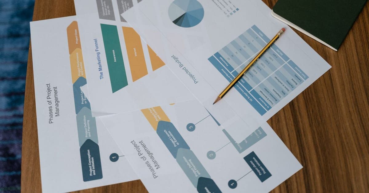 Printed charts and project management documents fanned out across a wooden desk
